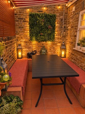 A brick wall with a green leafy wall panel, a black metal table, and two red benches. - DR15 - Stylish 2-Bed with Patio near Queen's Park (Greater London)