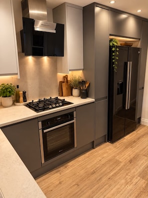 A modern kitchen with a built-in gas stove, oven, and a stainless steel refrigerator. - DR15 - Stylish 2-Bed with Patio near Queen's Park (Greater London)