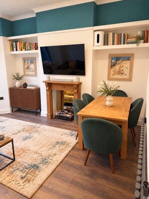 Een moderne woonkamer met een houten eettafel, groene stoelen, een flatscreen televisie, boekenkasten en een open haard.