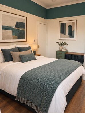 Een slaapkamer met een bed, nachtkastje, dressoir en twee ingelijste kunstwerken aan de muur.