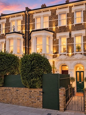 A row of terraced houses with bay windows, a green gate, and a brick wall. - DR15 - Stylish 2-Bed with Patio near Queen's Park (Greater London)