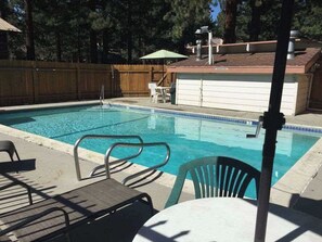 A swimming pool with a wooden deck, chairs, and a covered area. - Pet Friendly Mammoth Studio w/ self check in (Mammoth Lakes)