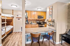 A compact kitchen with wooden cabinets, a microwave, and a stove. There is a small dining area with two chairs and a table. - Pet Friendly Mammoth Studio w/ self check in (Mammoth Lakes)
