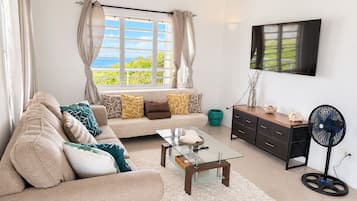 A living room with a sofa, coffee table, TV, and a fan.