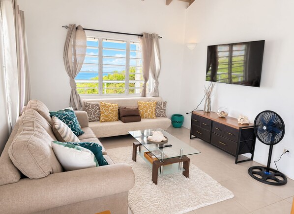 A living room with a sofa, coffee table, TV, and a fan.