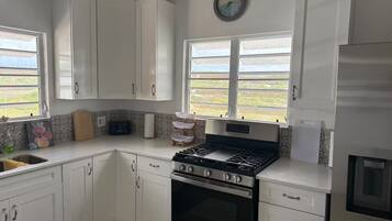 Une cuisine avec des meubles blancs, une cuisinière, un évier et une fenêtre donnant sur un beau paysage.