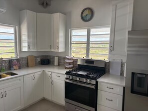 Une cuisine avec des meubles blancs, une cuisinière, un évier et une fenêtre donnant sur un beau paysage.