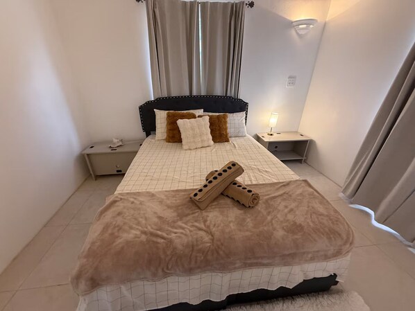 Une chambre à coucher avec un lit, des tables de chevet, une lampe et une fenêtre avec des rideaux.