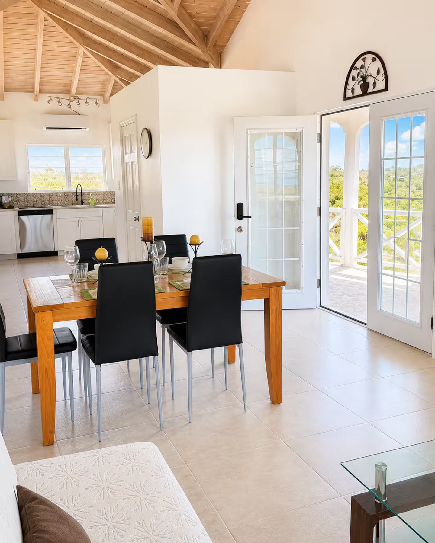 Un comedor con una mesa y sillas de madera, una cocina al fondo y vistas a través de un ventanal.