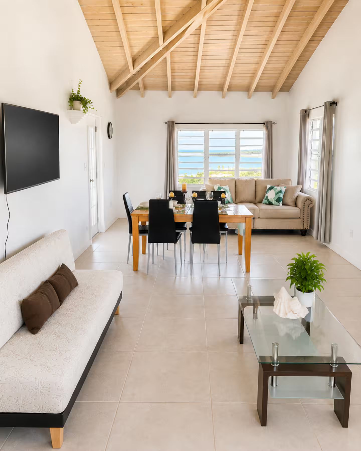 Un salon moderne comprenant un coin repas, un canapé, une table basse en verre et un téléviseur fixé au mur.