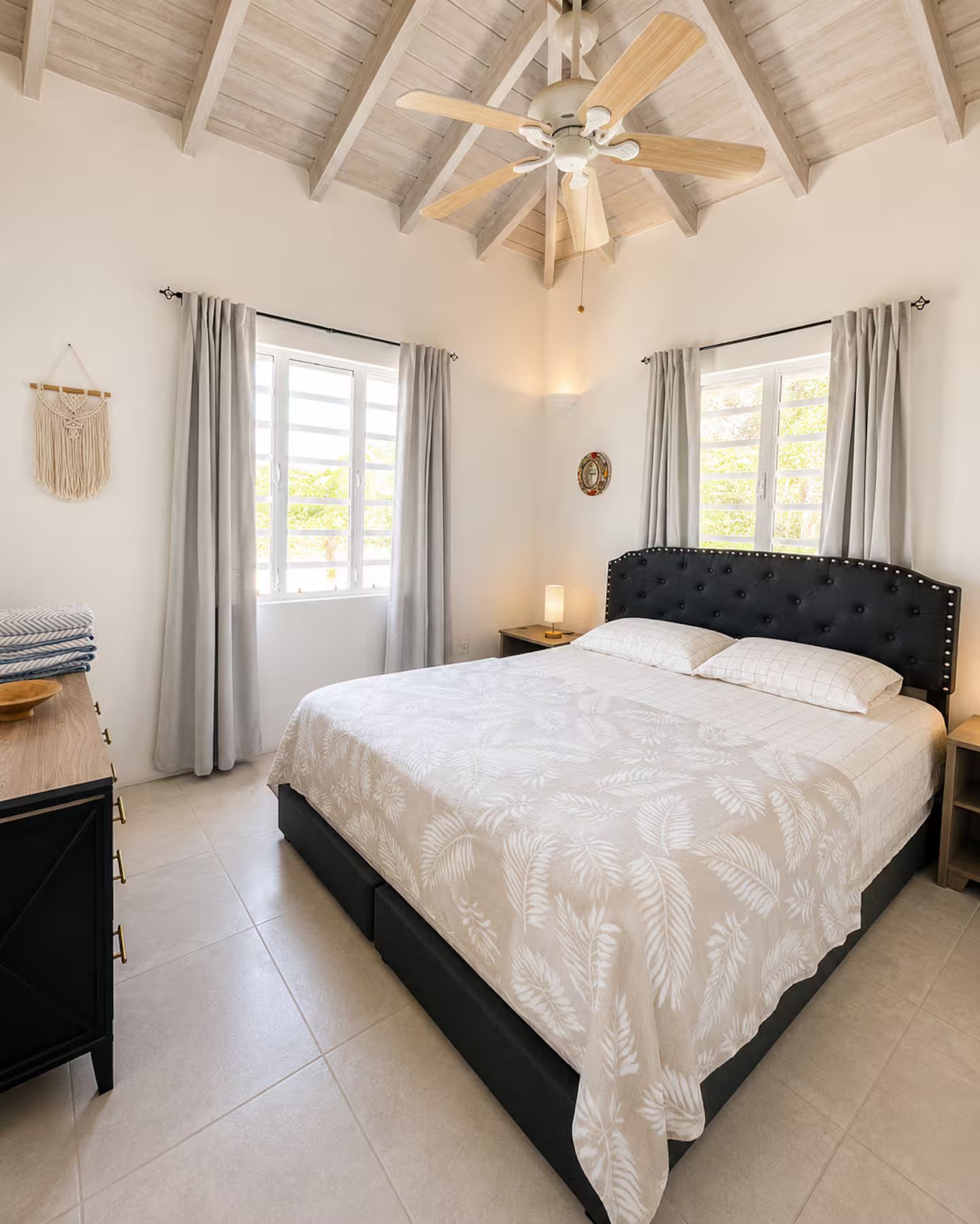A bedroom with a large bed, a ceiling fan, and two windows with curtains.