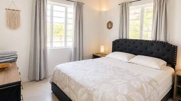A bedroom with a large bed, a ceiling fan, and two windows with curtains.