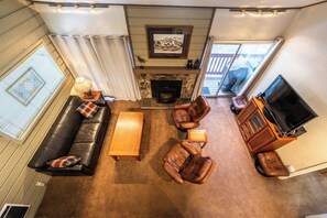 A living room with a fireplace, leather furniture, a television, and a window with curtains. - Mammoth Home-Away-From-Home (Mammoth Lakes)