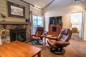A cozy living room with a stone fireplace, leather chairs, a wooden coffee table, and a television on a wooden stand. - Mammoth Home-Away-From-Home (Mammoth Lakes)
