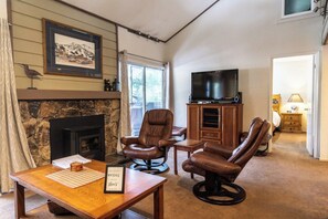 Uma sala de estar com lareira, poltronas de couro, televisão e parede de pedra.