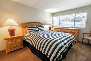 Quarto com cama, duas mesas de cabeceira, um criado-mudo, janela com persianas e uma cadeira.