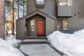 Une maison avec une porte rouge, un petit porche et un sol recouvert de neige.
