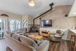 Un salon comprenant un canapé, des fauteuils, une table basse, une cheminée et un téléviseur fixé au mur.