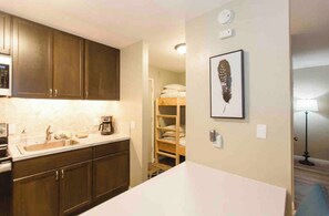 A compact kitchen with dark wooden cabinets, a white countertop, and a built-in oven. - Modern Pet friendly Studio with bunks (Mammoth Lakes)
