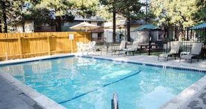 A rectangular swimming pool with a wooden fence, lounge chairs, and umbrellas. - Modern Pet friendly Studio with bunks (Mammoth Lakes)
