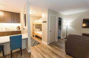 A compact living space with a kitchenette, a bunk bed, a sofa, and a lamp. - Modern Pet friendly Studio with bunks (Mammoth Lakes)