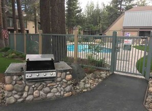 Een barbecue met een stenen onderstel, een zwembad en een toegangshek.