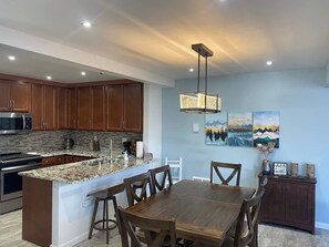 Een moderne keuken met granieten aanrechtbladen, houten keukenkastjes, een centraal kookeiland met barkrukken en een eettafel.
