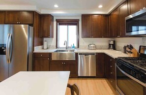 A modern kitchen with wooden cabinets, stainless steel appliances, and a white countertop. - Mammoth Mountain Townhome w/ Garage EV Charger (Mammoth Lakes)