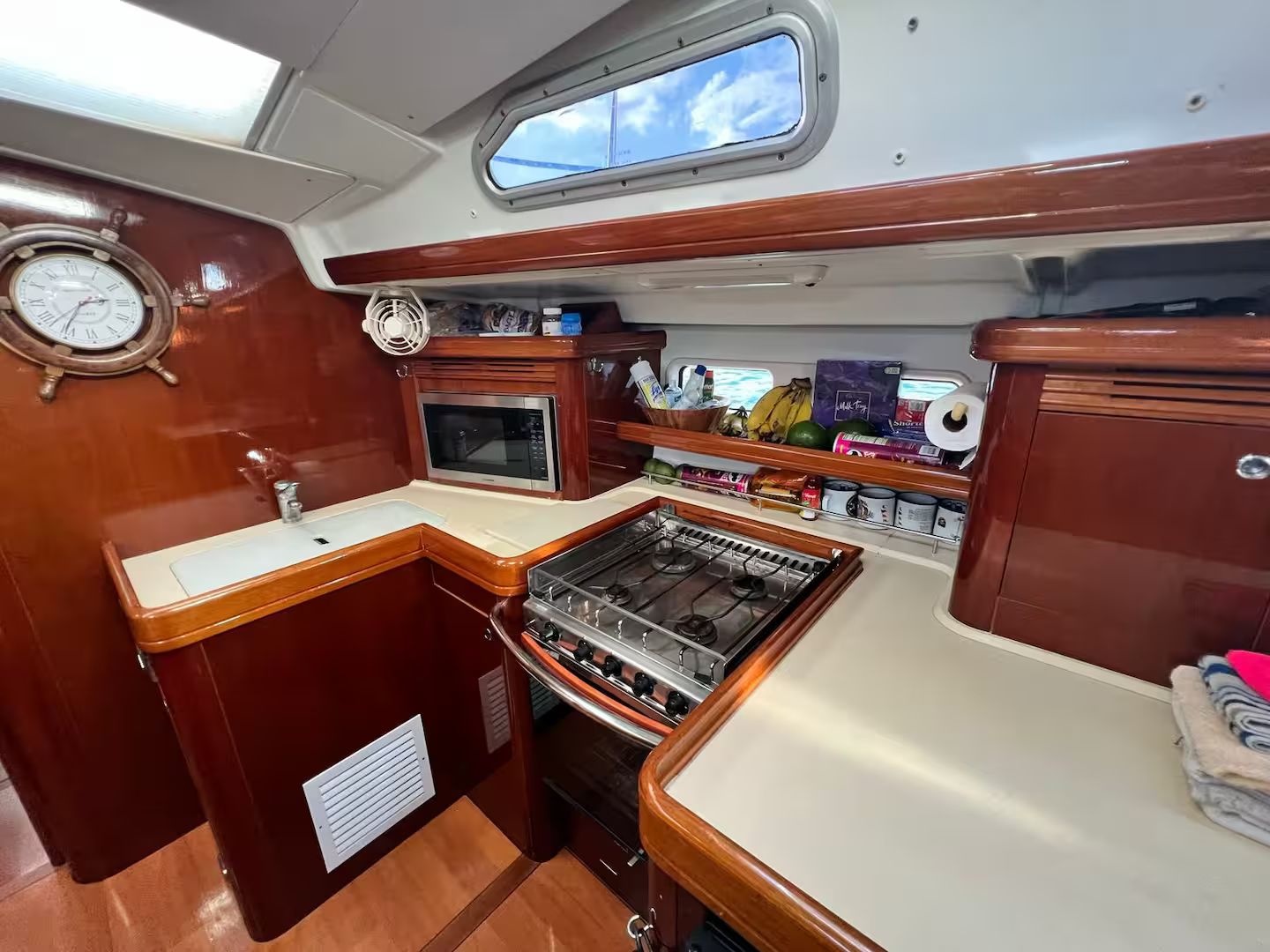 A compact galley with a stove, microwave, and sink, wooden cabinetry, and a clock on the wall.