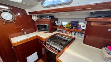 A compact galley with a stove, microwave, and sink, wooden cabinetry, and a clock on the wall.