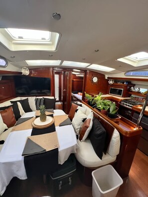 Interior de un yate con comedor, cocina y zona de estar con vistas al mar.
