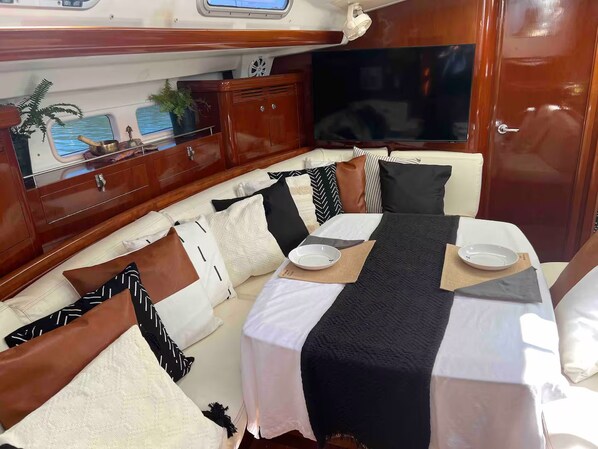 Cabina de barco con comedor que incluye una mesa dispuesta con platos, un televisor y muebles de madera.