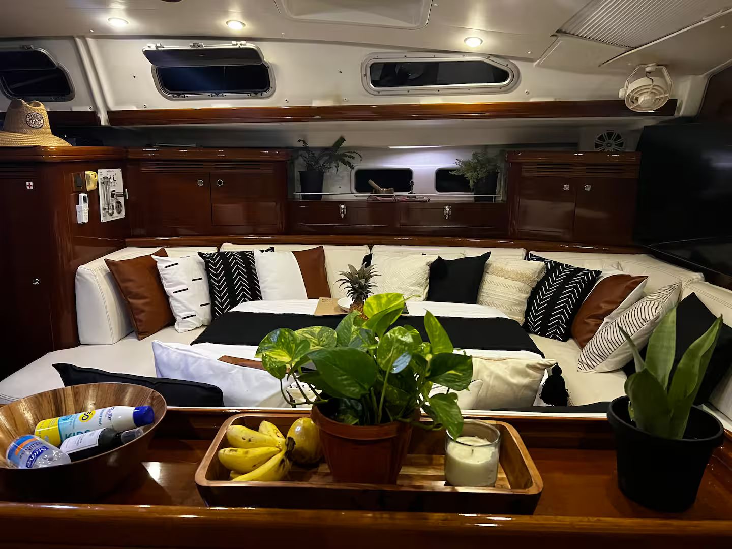 A boat cabin with a sofa, pillows, a tray with food and drinks, and a potted plant.