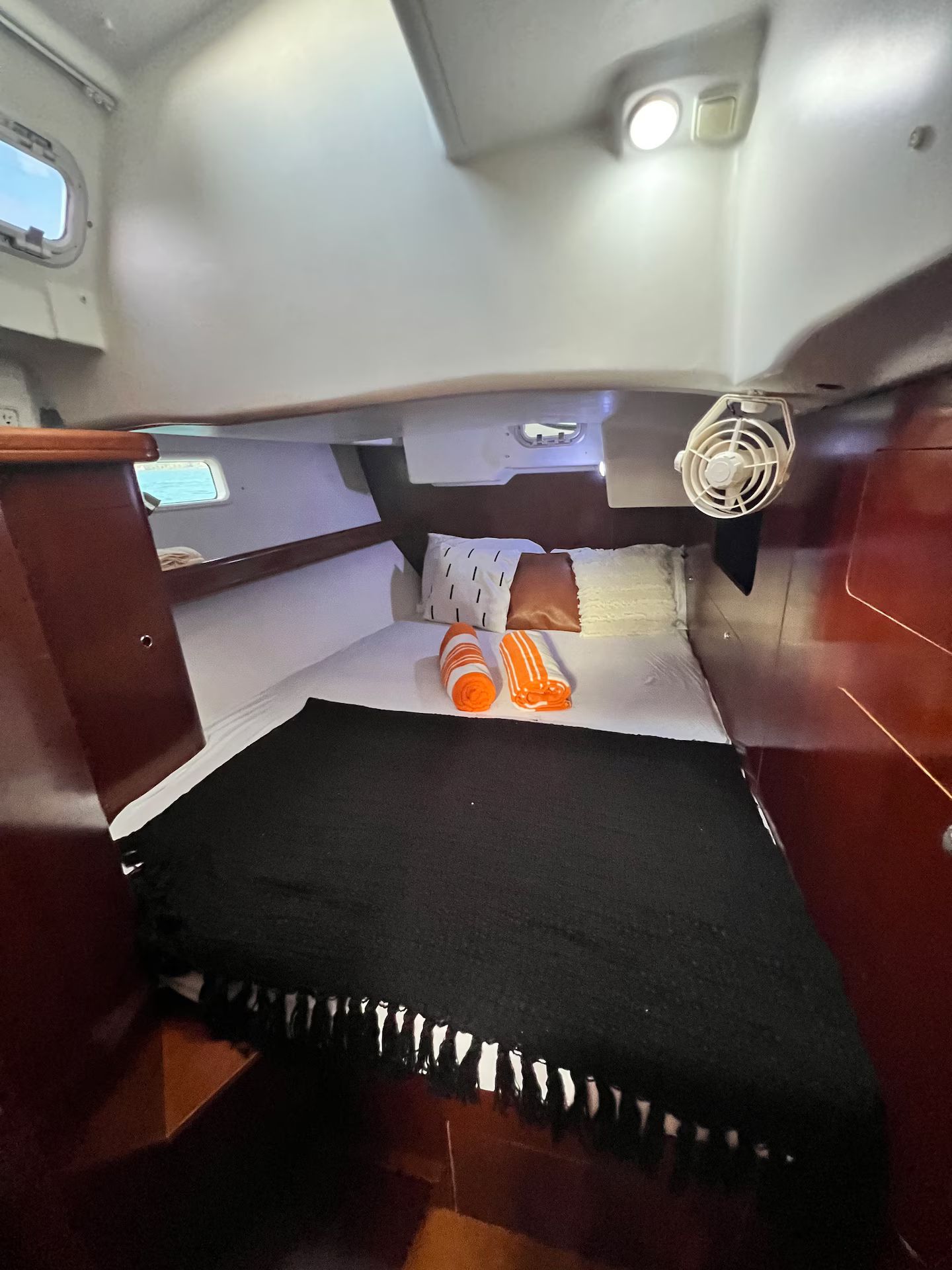 Um quarto pequeno com cama, travesseiros e um ventilador.