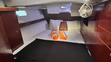 Um quarto pequeno com cama, travesseiros e um ventilador.