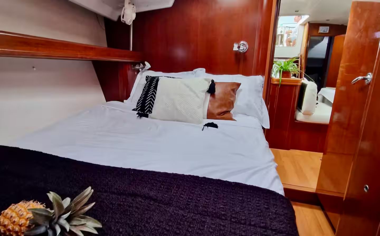 Una cama con sábanas blancas, un plaid oscuro y una piña a un lado.