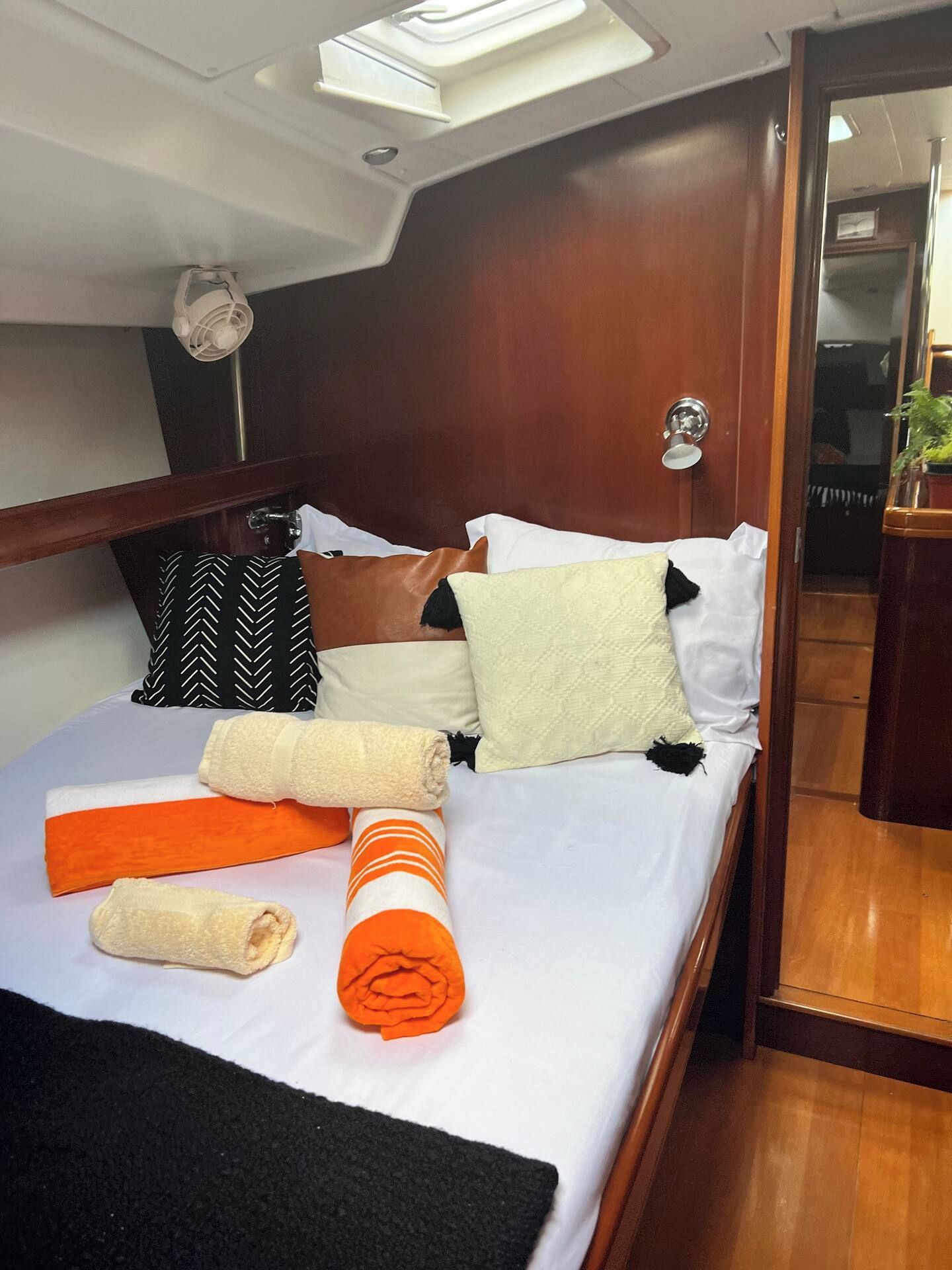 A neatly made bed with pillows and rolled towels in a cabin with a wooden headboard and a skylight above.