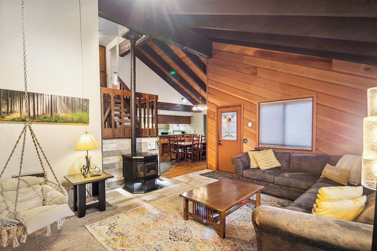 A cozy living room with a sofa, a coffee table, a hanging chair, a fireplace, and a staircase leading to an upper level.