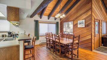 A wooden interior with a dining table and chairs, a kitchen area, and a window with curtains.
