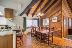 A wooden interior with a dining table and chairs, a kitchen area, and a window with curtains.