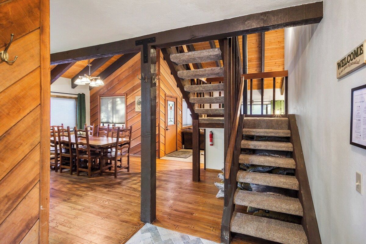 A wooden interior with a staircase, a dining area with chairs, and a welcome sign.