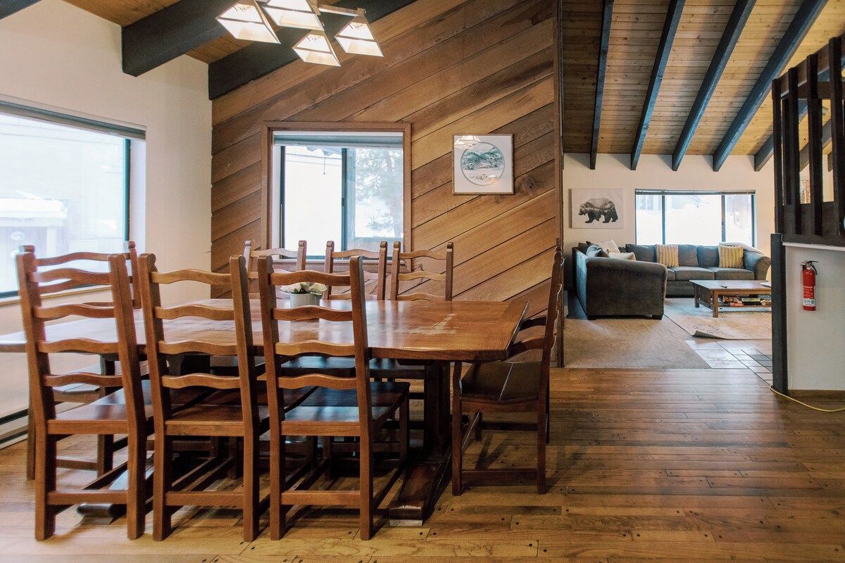 A dining area with a wooden table and chairs, a sofa, and a fireplace.