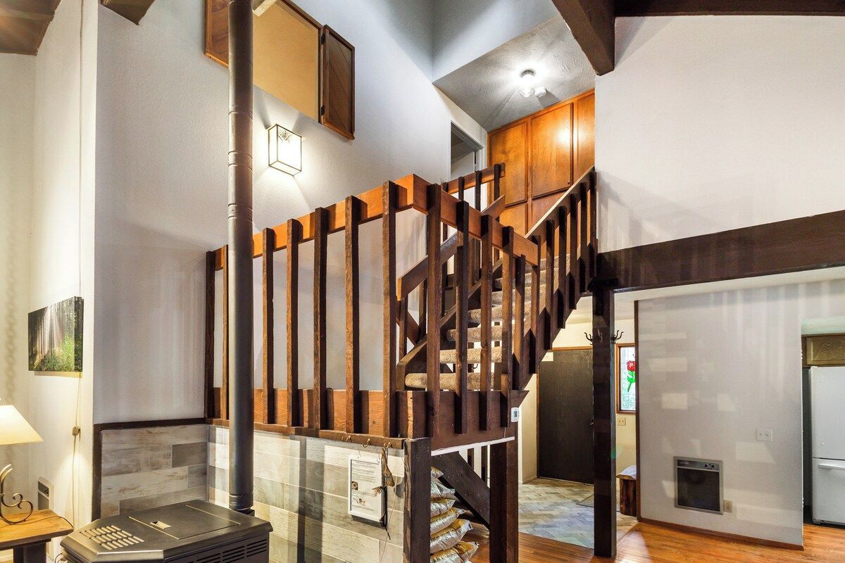 A staircase with wooden railings leading to an upper level, a fireplace, and a modern kitchen area.