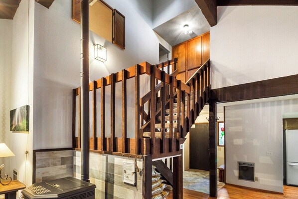 A staircase with wooden railings leading to an upper level, a fireplace, and a modern kitchen area.