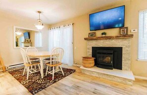A dining area with a table and chairs, a fireplace, a mounted television, and a window with curtains. - Mammoth Horizon 4 1BD 1BA Family Getaway (Mammoth Lakes)