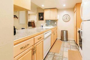 A compact kitchen with wooden cabinets, a stainless steel trash bin, and a clock on the wall. - Mammoth Horizon 4 1BD 1BA Family Getaway (Mammoth Lakes)