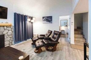 A living room with a stone wall, a fireplace, a TV, and a staircase leading upstairs. - Pet Friendly 1BR loft 2BA Modern Mammoth Condo (Mammoth Lakes)