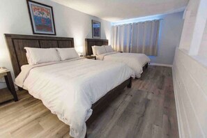 Een hotelkamer met twee bedden, een houten hoofdbord, een nachtkastje en een raam met gordijnen.