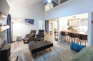 A spacious living area with a fireplace, leather chairs, a dining table with chairs, and a kitchen visible through an open doorway. - Pet Friendly 1BR loft 2BA Modern Mammoth Condo (Mammoth Lakes)