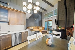 A modern kitchen with wooden cabinets, a dining area with a table and chairs, and a fireplace. - Mammoth Mountain 3BR 3BA Beautiful Family Getaway (Mammoth Lakes)